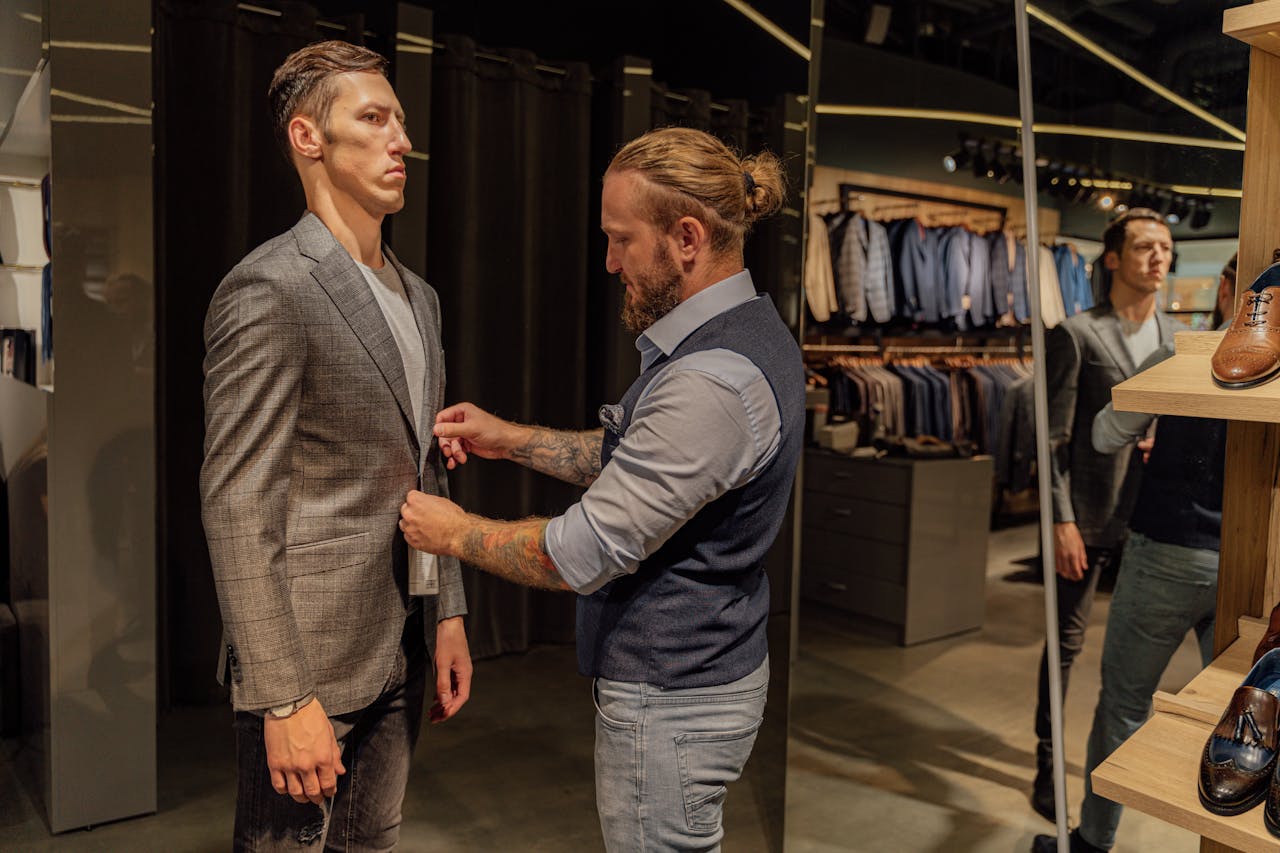 A tailor adjusts a man's suit jacket in a modern fashion store.